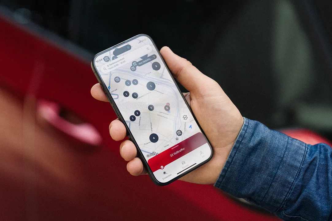 Hand hält Smartphone mit Mobility-App zur Suche und Buchung eines Carsharing-Fahrzeugs.