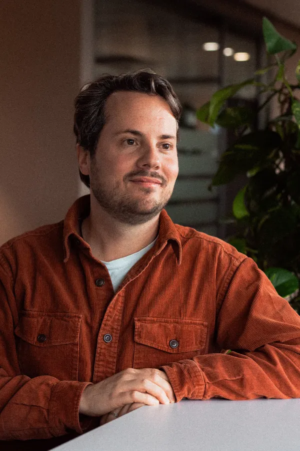 Markus Broder sitzt an einem Tisch im Büro und blickt lächelnd zur Seite.